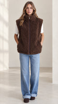 Front view of woman wearing brown sherpa fleece zip-up vest with jeans