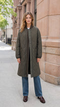 Front full-length view of model wearing olive green longline quilted bomber coat with blue jeans