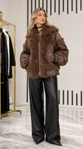 Full front view of model wearing brown faux leather and plush shearling paneled bomber jacket with black wide-leg trousers